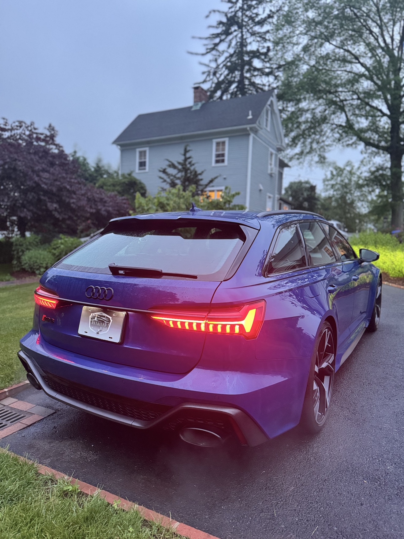 Blue Audi RS6 Avant rear three-quarter view with glowing taillights and Detailed by Yael plate frame