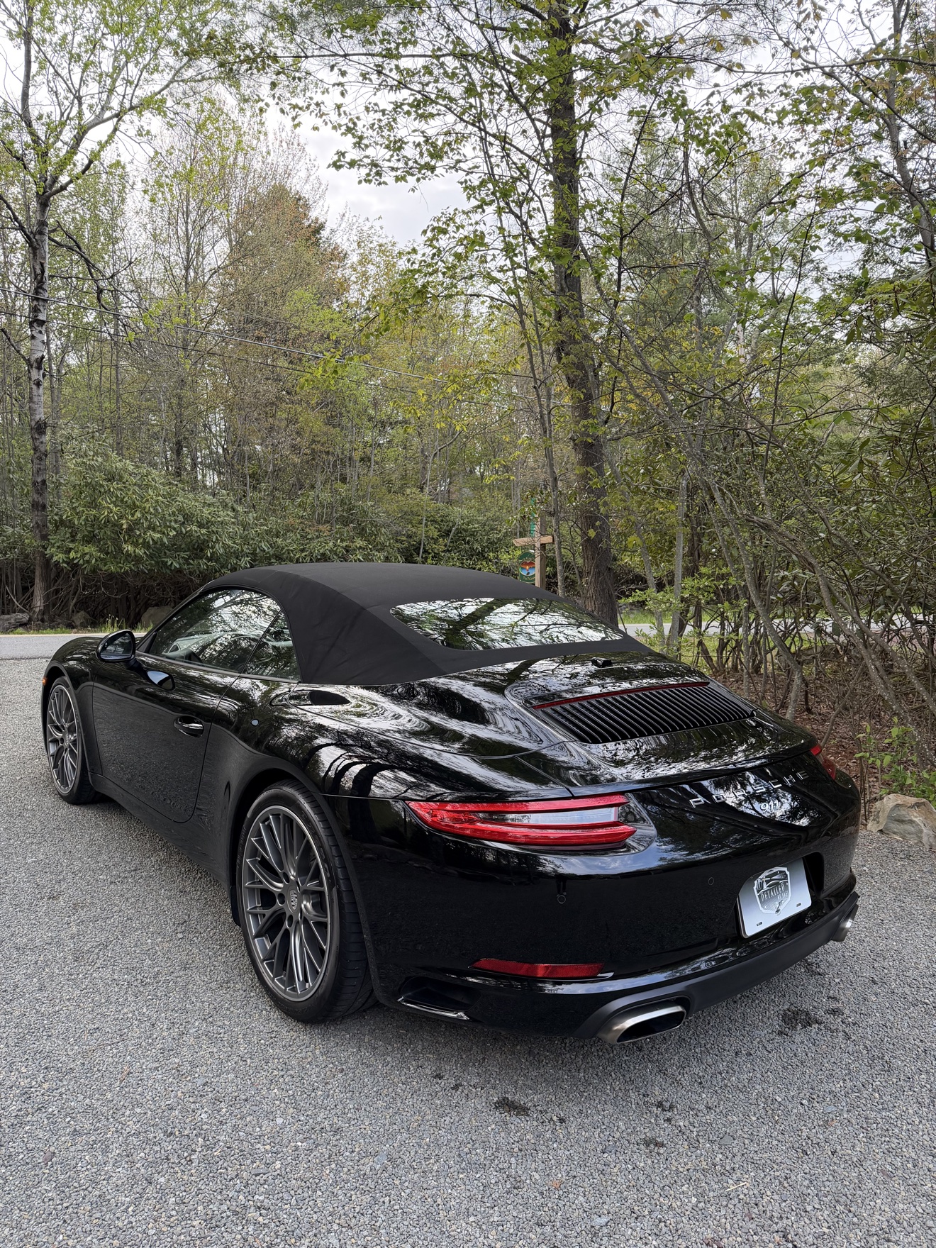 Black Porsche 911 Carrera Cabriolet rear three-quarter view with soft top up and Detailed by Yael plate frame