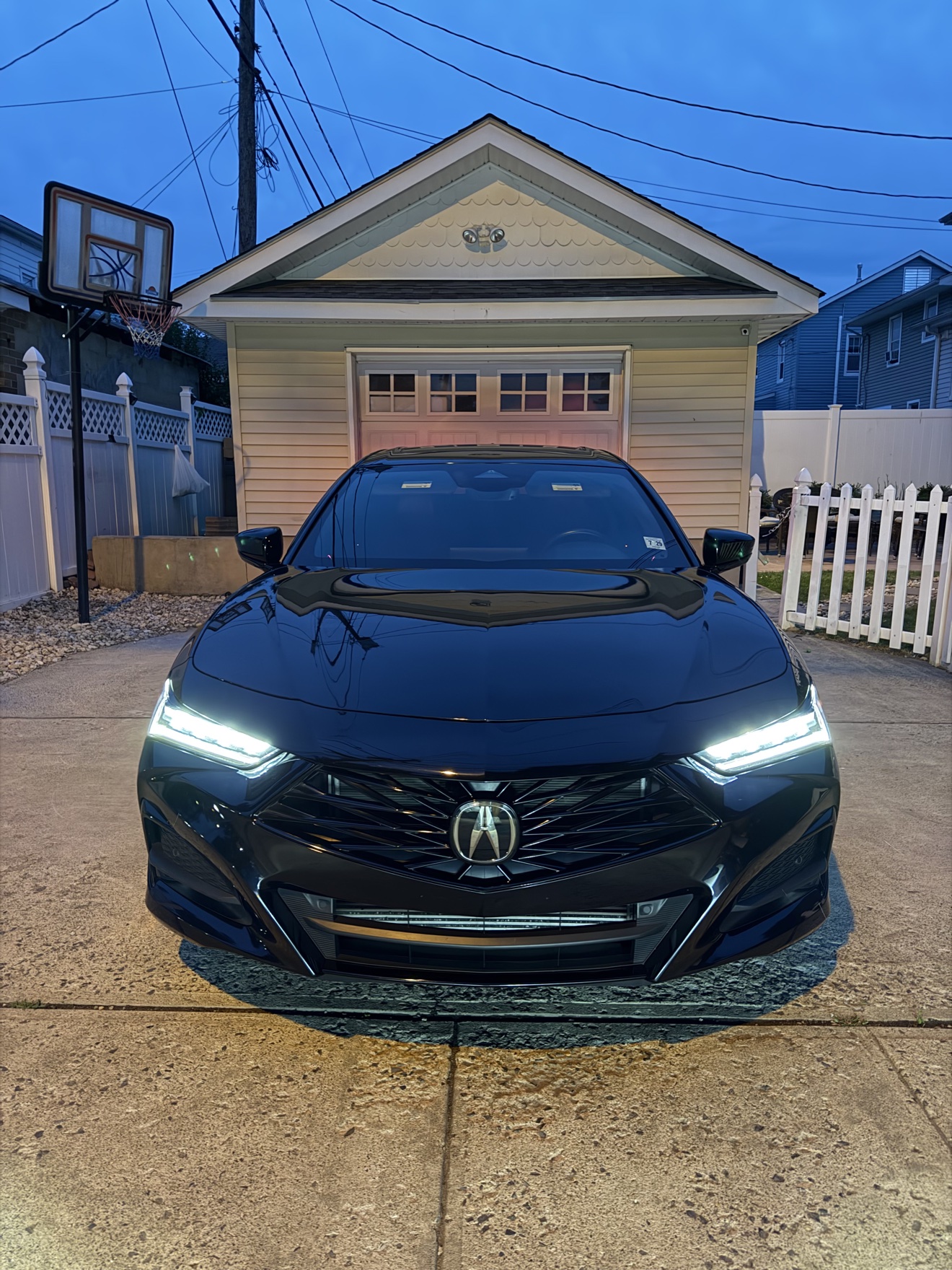 Front view of a black Acura TLX SH-AWD A-Spec with headlights on